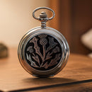 Silver pocket watch with a black and white floral design on a white background